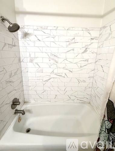 A white bathtub with a shower head and a white tiled wall.