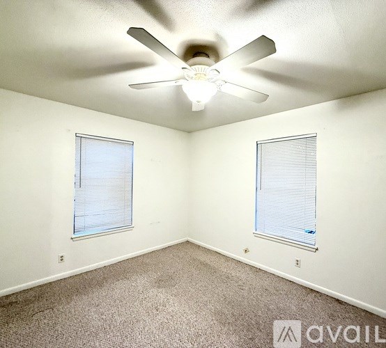 A room with a ceiling fan and two windows.
