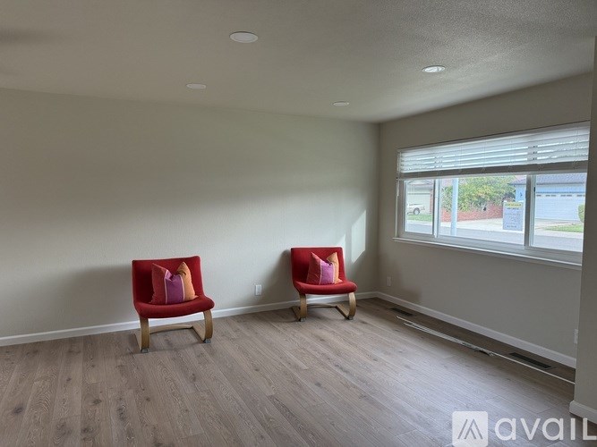 Two red chairs are placed in a room with wooden flooring and a window.