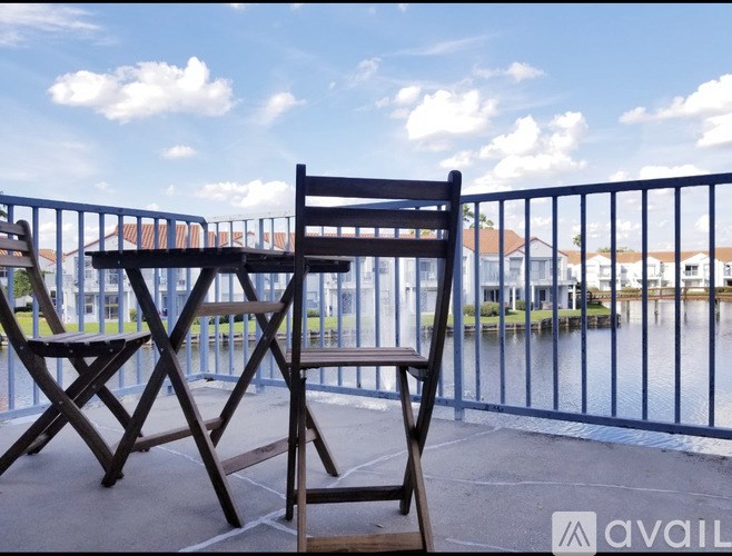 A wooden chair is on a balcony with a view of a body of water and houses.