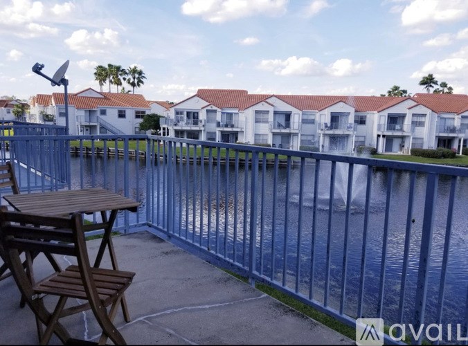 A patio with a table and chairs overlooks a body of water with houses in the background.
