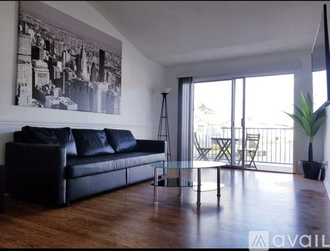 A black leather couch sits in a living room with a large window and a plant.