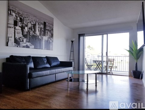 A black leather couch sits in a living room with a large window and a plant.