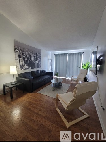 A living room with a black couch, a white chair, and a wooden floor.