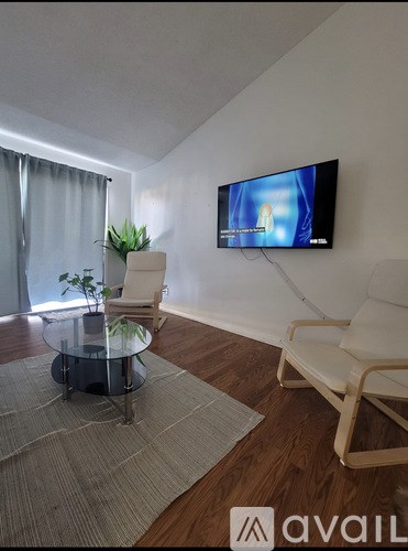 A living room with a television, a glass coffee table, and two chairs.
