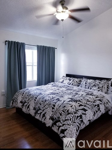 A bedroom with a bed, a ceiling fan, and a window with curtains.