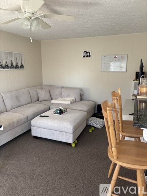 A living room with a grey couch, a wooden chair, and a small table with a bottle on it.