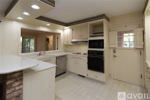 A kitchen with white cabinets and appliances, a brick wall, and a window.