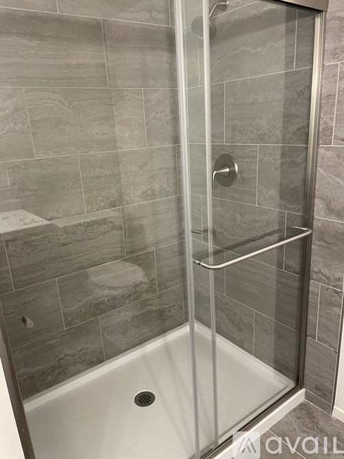 A shower with a glass door and a grey tiled wall.