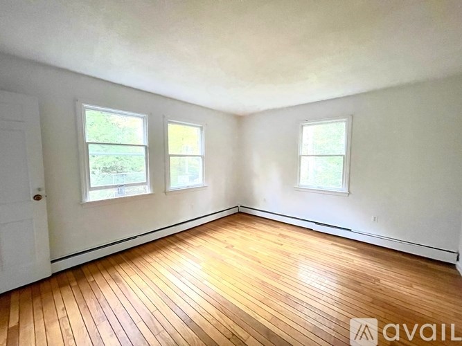 A room with wooden flooring and three windows.