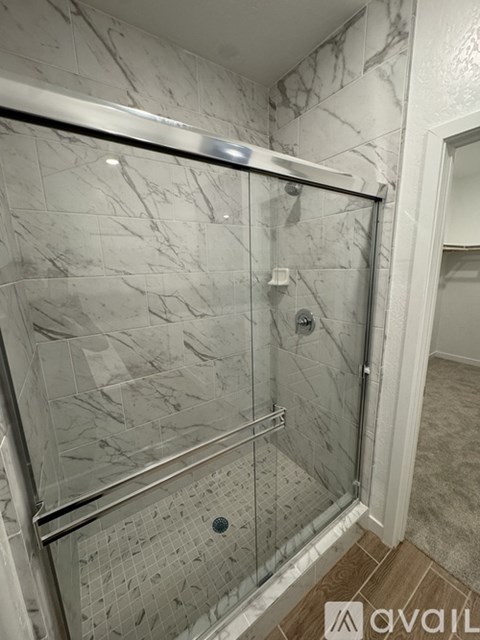A shower with a glass door and a marble wall.