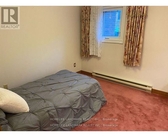 A bedroom with a bed covered in a grey comforter and a window with curtains.
