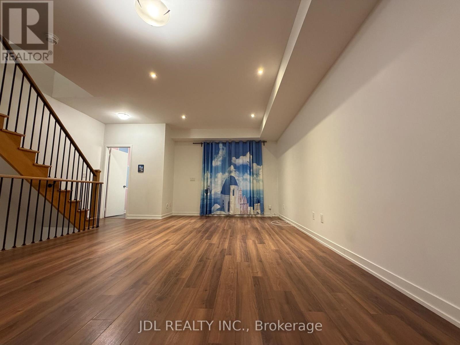 A spacious room with wooden flooring and a staircase with a railing.