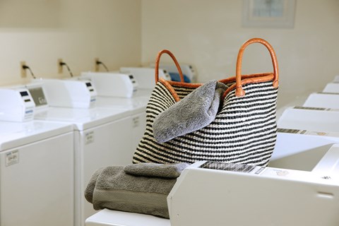 A striped bag with orange handles is filled with towels and is placed on top of a washing machine.
