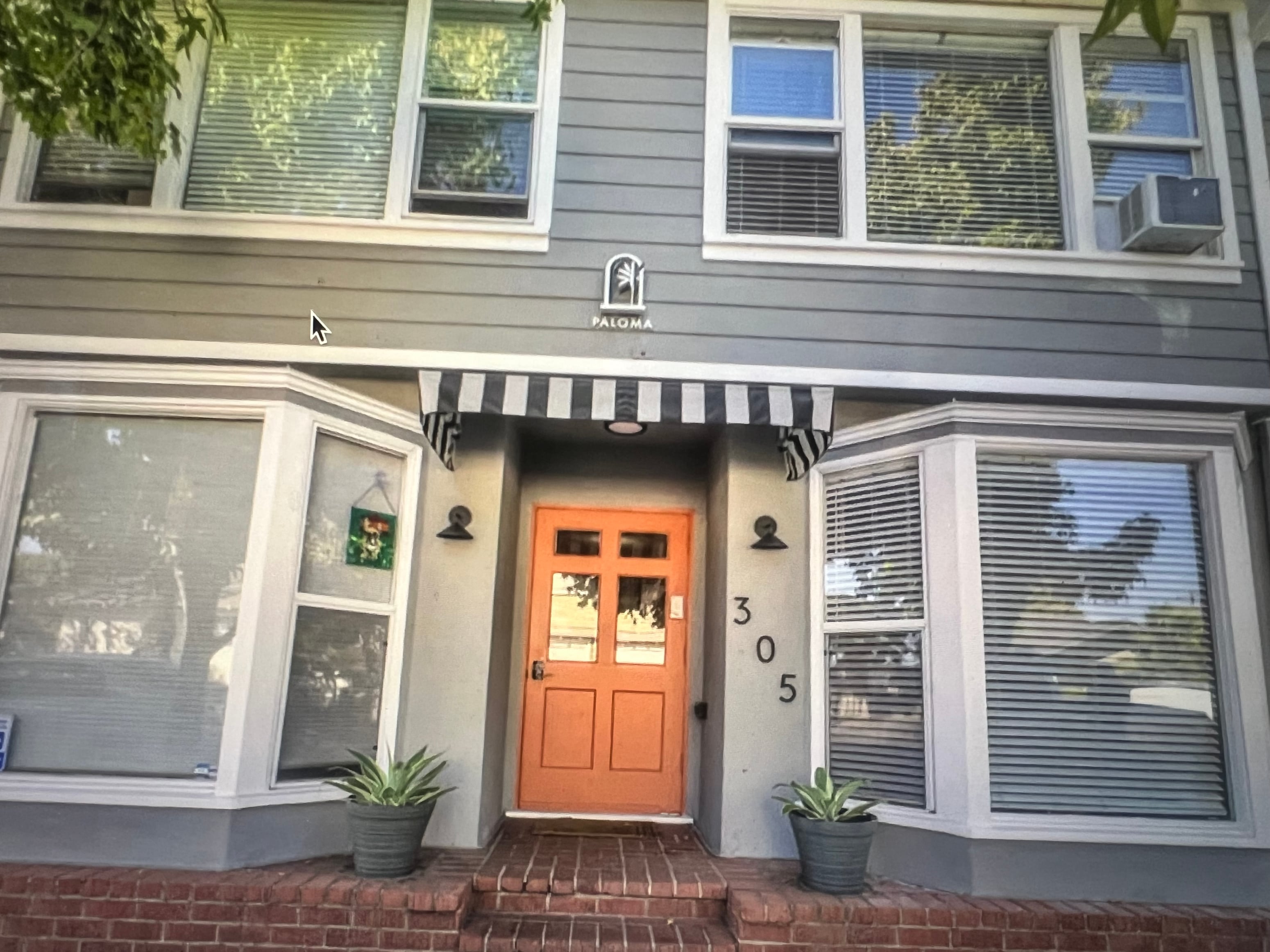 A grey house with a black and white striped awning and a red door.