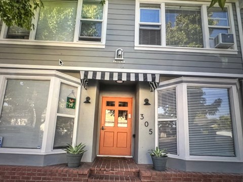 A grey house with a black and white striped awning and a red door.