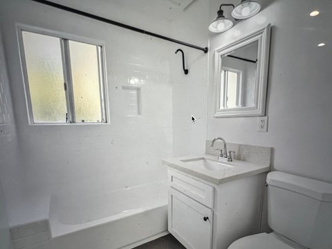 A white bathroom with a sink, mirror, and bathtub.