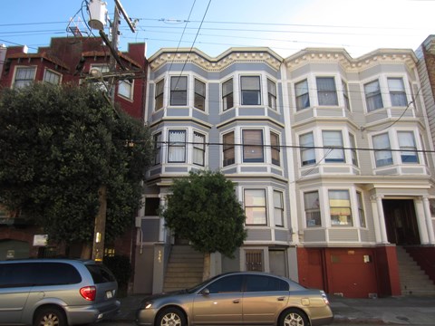 A row of houses with cars parked in front.