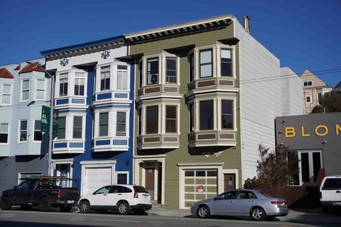 A row of colorful houses with cars parked in front.