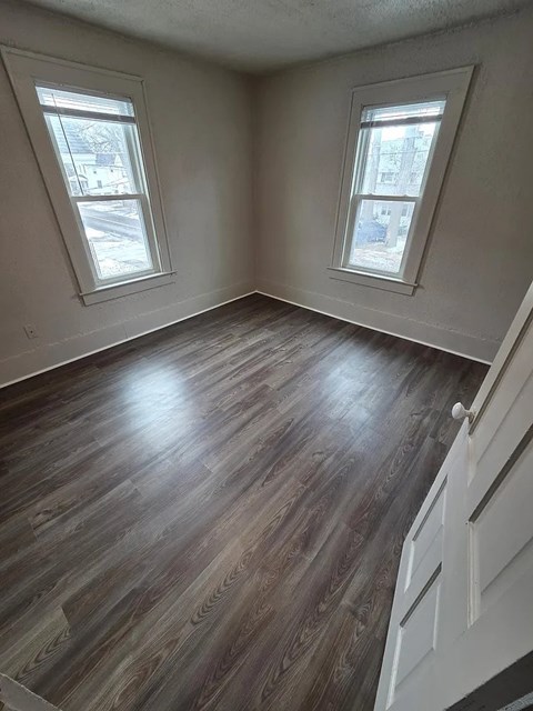 A room with wooden flooring and two windows.