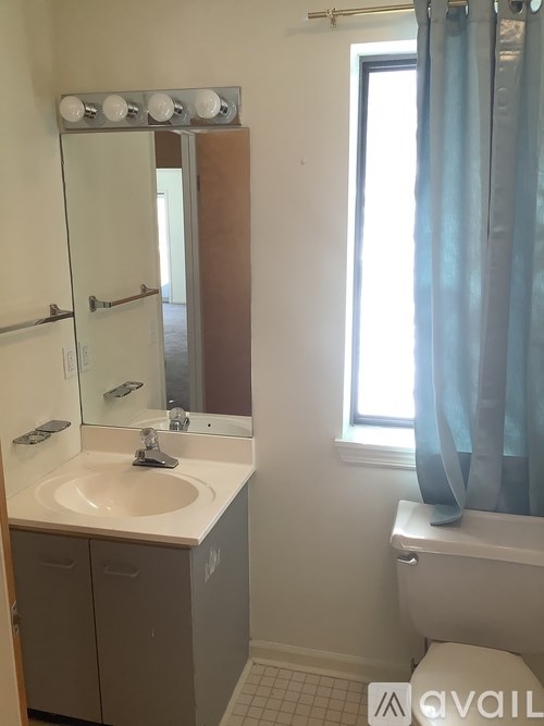 A bathroom with a sink, mirror, toilet and a window with a blue curtain.
