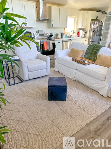 A living room with a white couch and a white chair with a plant in the corner.