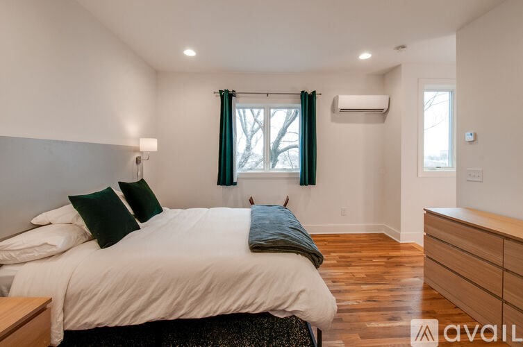 A person is kneeling on a bed in a bedroom with a window and a dresser.