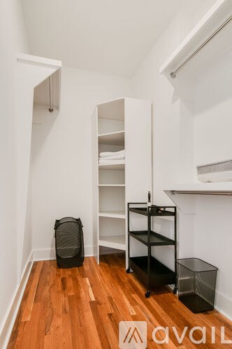 A room with a wooden floor and a white wall with a cabinet and a black bag.