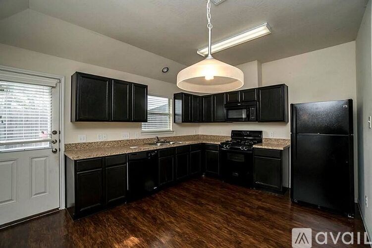 A kitchen with black cabinets and appliances, a granite countertop, and a wooden floor.