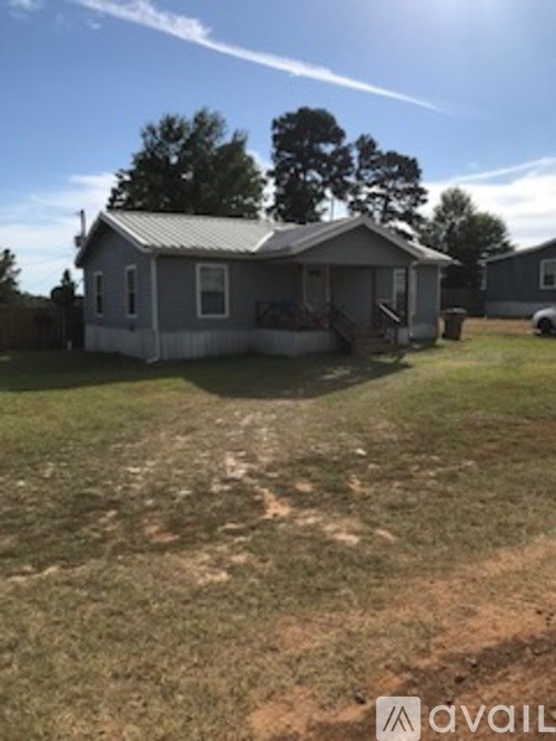 A house with a grey roof and a porch is surrounded by a grassy yard.
