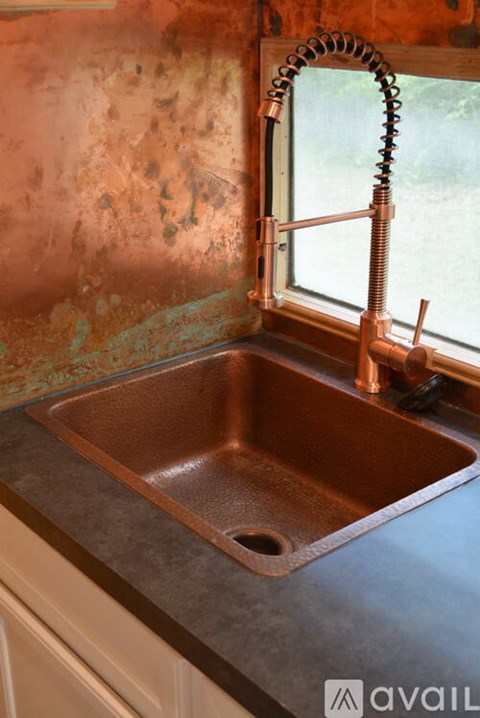 A copper sink in a kitchen with a window above it.