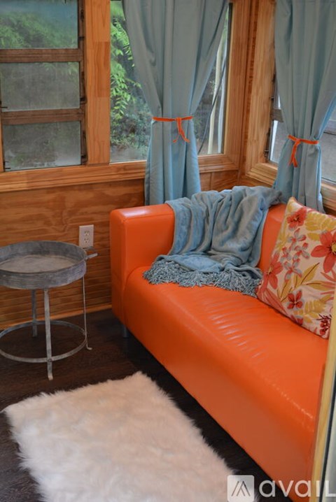 A bright orange couch with a round table and a white rug in front of a window.