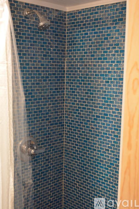A shower with a blue tiled wall and a white curtain.