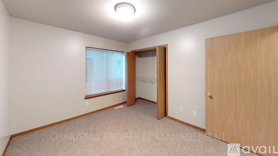 A bedroom with a carpeted floor, a window with a view of a building outside, and a wooden door.