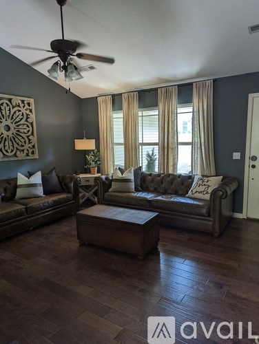 A living room with a brown leather couch, a wooden coffee table, and a ceiling fan.