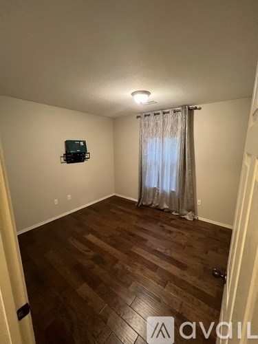 A room with wooden flooring and a window with curtains.