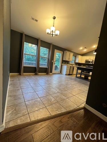 A living room with a chandelier and a kitchen in the background.