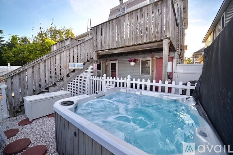 A hot tub is in the middle of a gravel area with a deck and a fence around it.