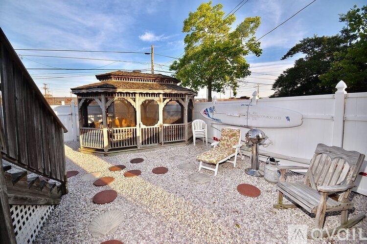 A gazebo is surrounded by a white fence and chairs.