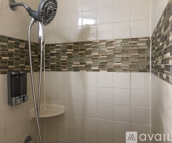 A shower with a glass tile wall and a white tub.