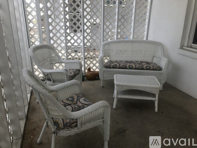 Two white wicker chairs with cushions are placed on a patio.