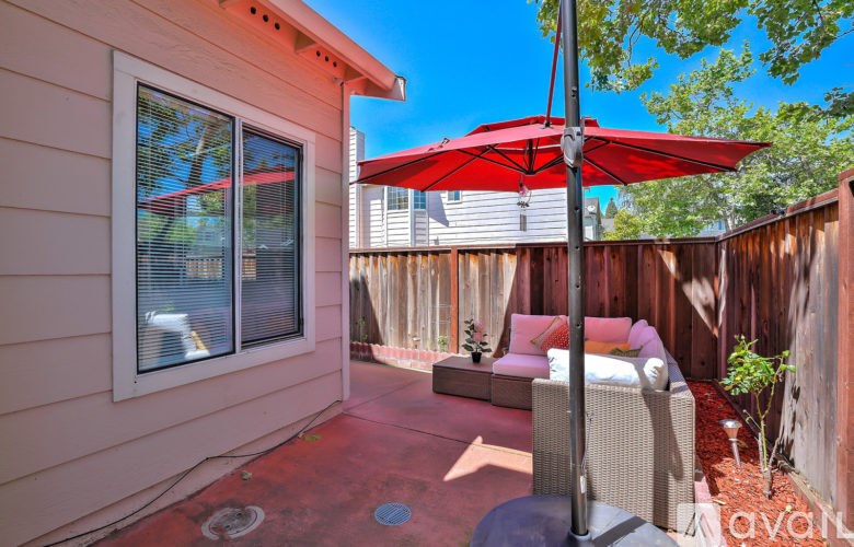A patio with a red umbrella and a couch.