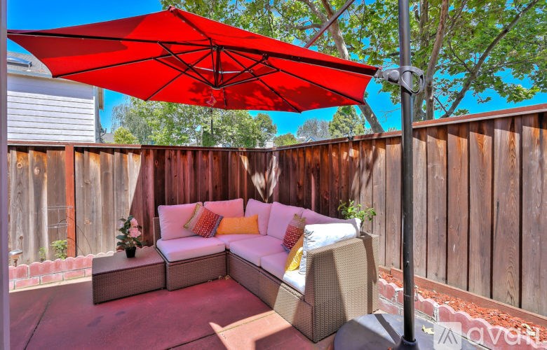 A red umbrella shades a white couch and table on a patio.