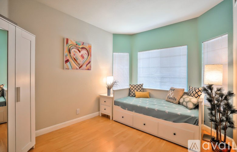 A bedroom with a bed, nightstand, and a heart-shaped painting on the wall.