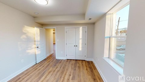 A room with white walls and wooden flooring, with a large window on the right side.
