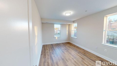 A room with wooden flooring and white walls, with a window on the right side.