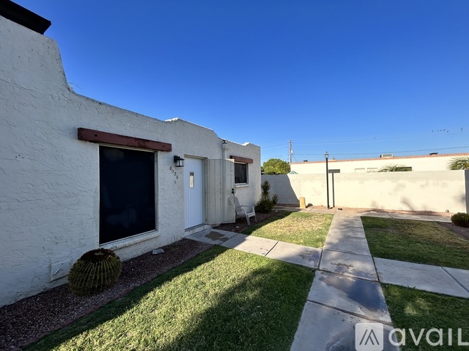 A white house with a brown window trim and a cactus in front.