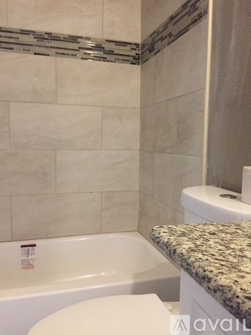 A white toilet sits in a bathroom with a marble counter top and a tiled wall.