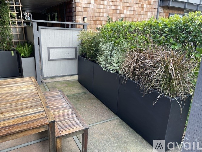 A wooden table and bench are in front of a grey planter box.