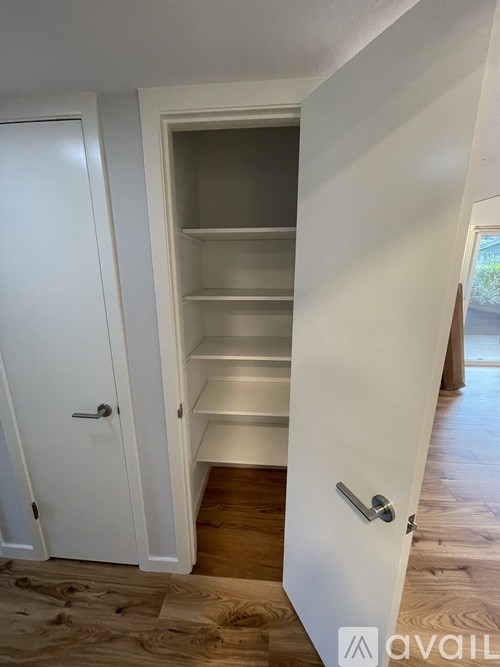 A white door with a handle is open to a small pantry with shelves.
